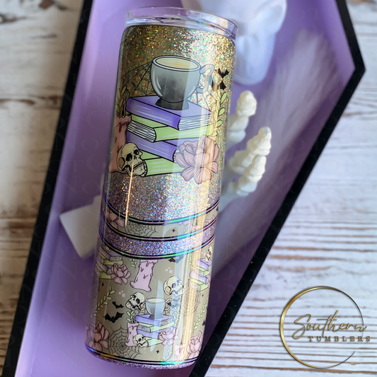 20oz skinny tumbler decorated with green and purple ombre glitter, skull heads, candles, books, bats, spider webs and flowers