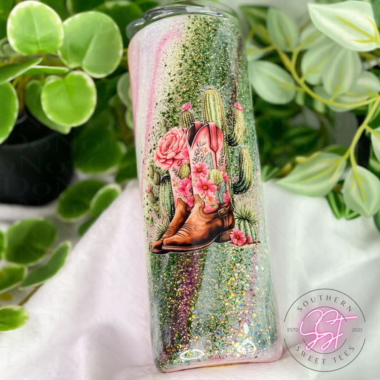 20oz skinny straight tumbler decorated with pink, green and white glitter with a milky way effect and an image of western cowboy boots and cactus flowers