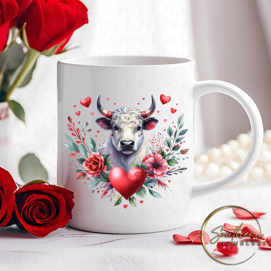 11oz drinking mug sublimated with an image of a highland cow surrounded by a heart shaped floral arrangement and hearts