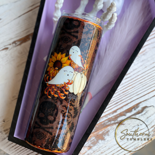 20oz skinny tumbler decorated with orange glitter wrapped in skeleton fabric with a decal of a sunflower and ghosts saying stay spooky