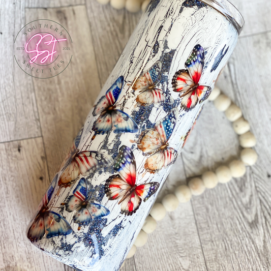 20oz skinny straight tumbler decorated with blue glitter underneath crackling paint and patriotic butterflies