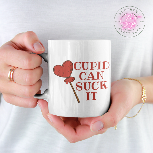 11oz white drinking mug with the sarcastic saying cupid can suck it and the image of a red heart shaped lolly pop 