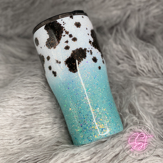 20oz modern curved tumbler decorated with white and teal colored glitter and cow print spots added with black alcohol ink